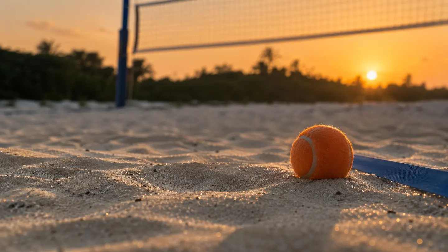 Bola laranja de beach tennis na areia ao lado da linha azul da quadra, com a rede alta ao fundo.