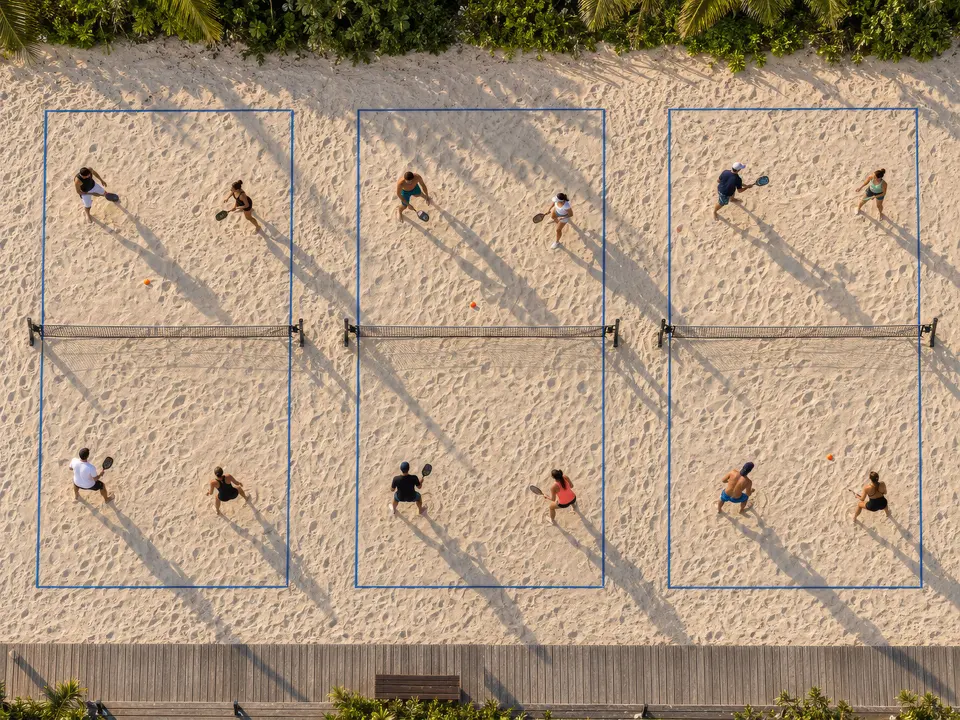 Três quadras de beach tennis lado a lado vistas de cima, com linhas azuis na areia.